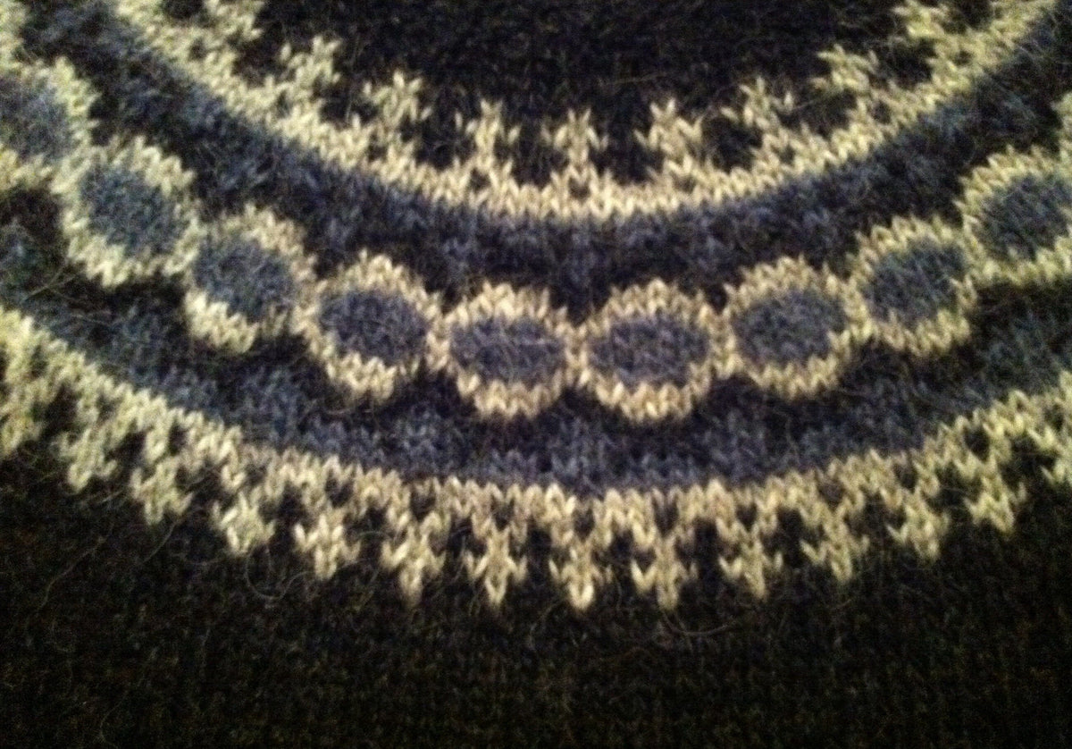 Close-up of the yoke of the Léttlopi vest, in the pattern’s colours — small ash crosses on black, a stone blue band, a band of stone blue dots framed in ash, another stone blue band and ash crosses towards the neck
