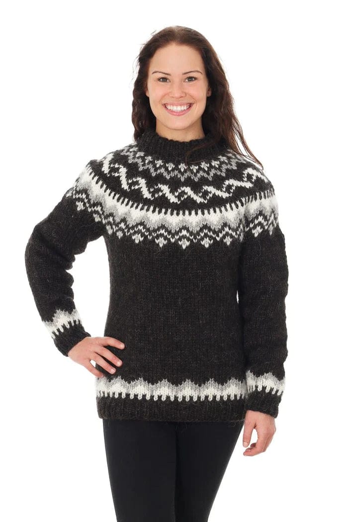 Smiling dark-haired woman against a white background in a sweater knitted from the Lopi 12 no. 14 pattern — a dark body and sleeves, the white and light grey yoke and border, and a high folded neckband. The black leggings are not part of the pattern