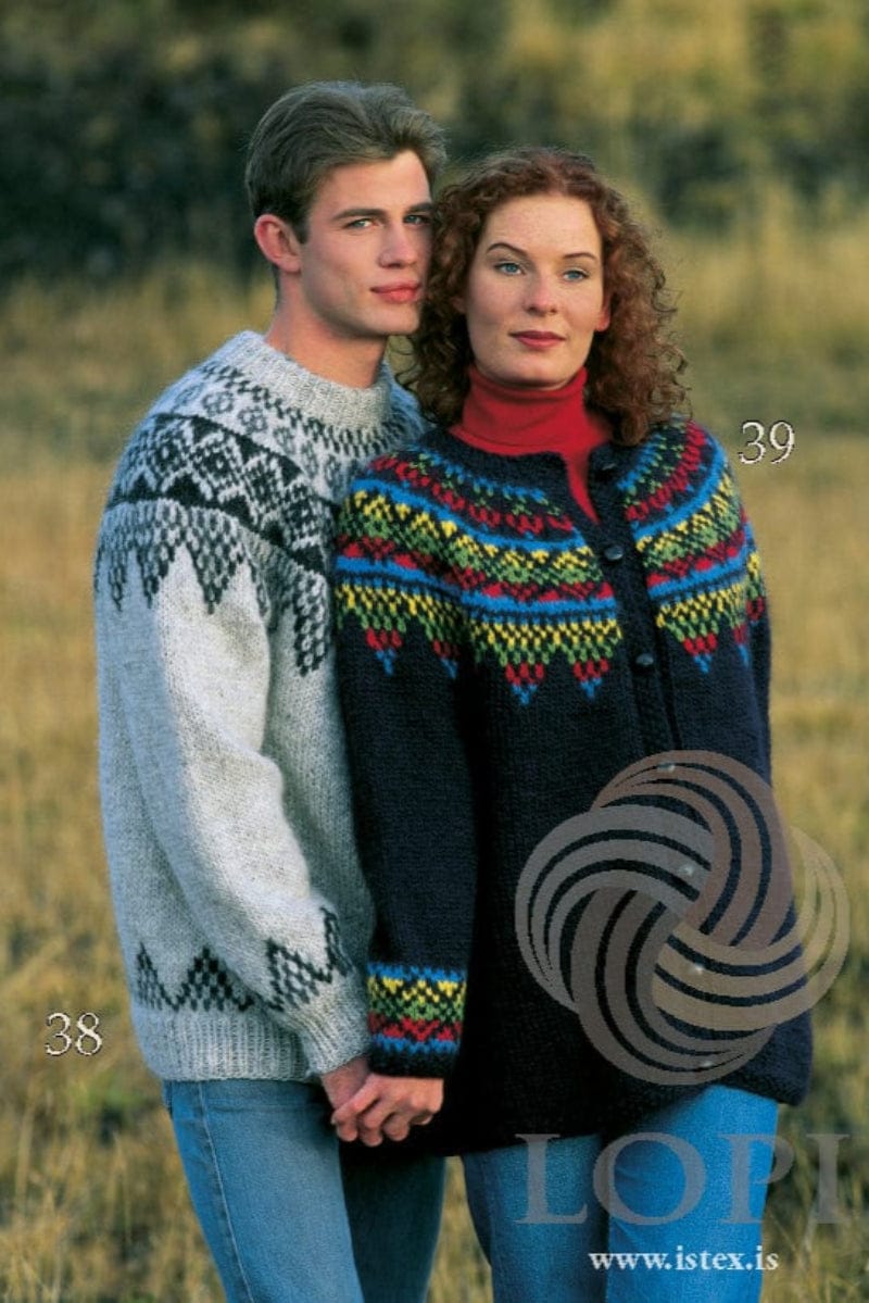A man and a red-haired woman in a field of dry grass, in the pattern’s original colours; 38 and 39 are printed beside them. He wears No. 38, a light grey pullover with black heather and dark gray zigzags on the yoke and above the hem and cuff ribs. She wears No. 39, a midnight blue cardigan with pointed bands of blue, red, green and yellow on the yoke and cuffs, and dark buttons; four of its colours are no longer made. The jeans and her red polo neck are not part of the pattern; the buttons are not included