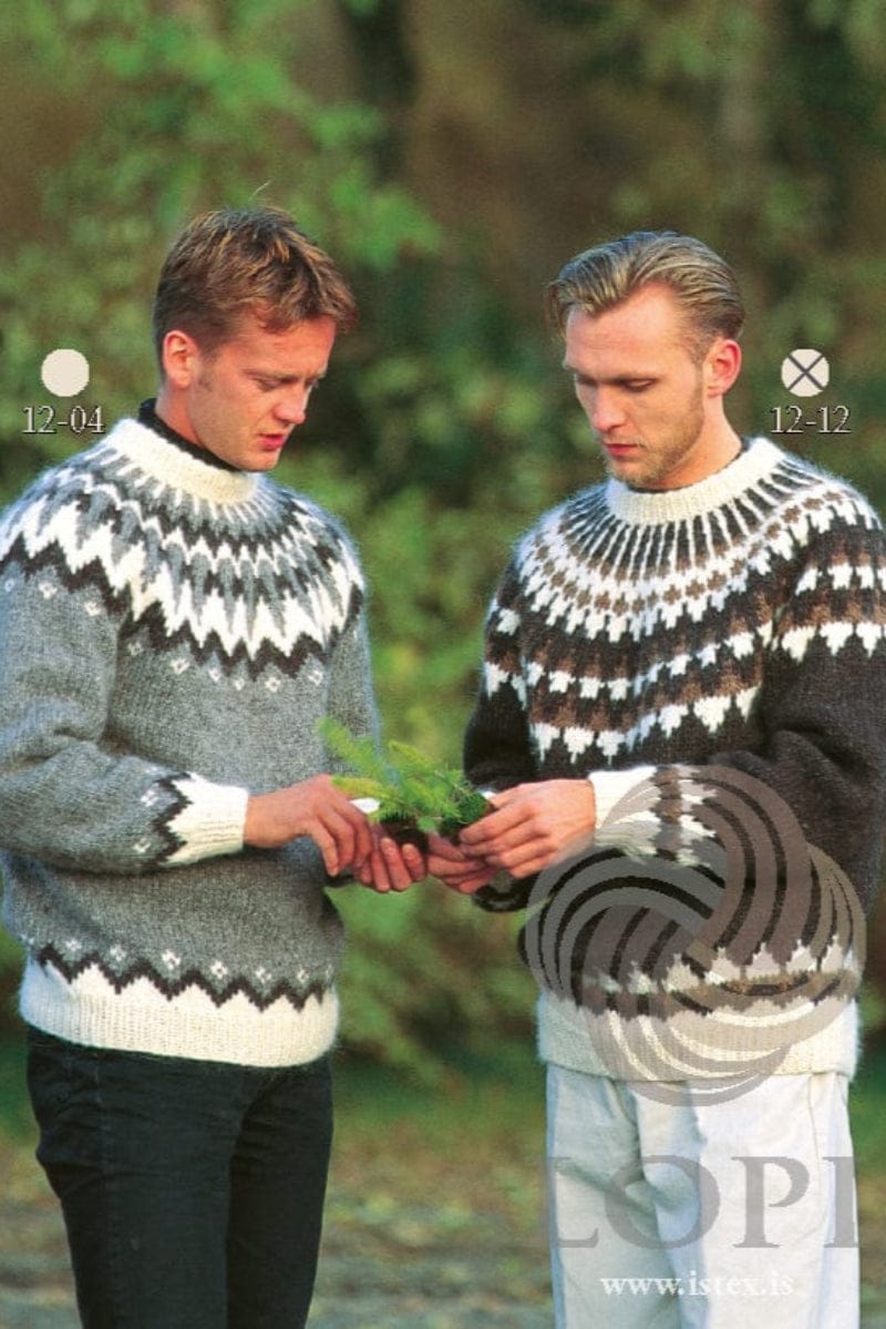 Two men looking down at a small plant. The man on the right, marked “12-12”, wears No. 12, the dark brown version of this pattern, in its own colours — black sheep with white rib, an acorn band and white triangles above the rib, a yoke of white triangles and acorn points, and white rays up to a folded white neckband. His light trousers and the plant are not part of the pattern; the man on the left wears Lopi 12 no. 4 (a different pattern), a black polo neck and black trousers. A LOPI logo is over the photo