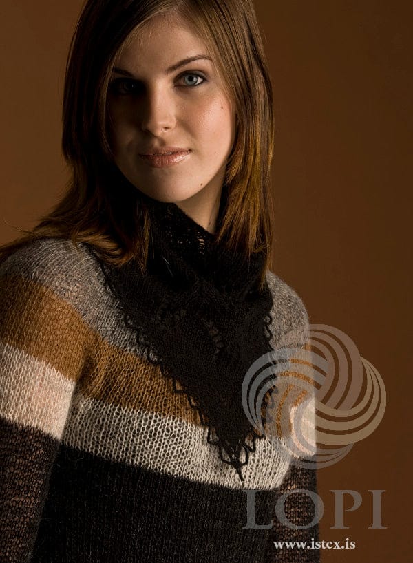 Woman wearing Blaka round her neck with the point hanging down at the front, shown in the pattern’s own colour, black Einband — the eyelet lace and the crocheted chain loops along the two sloping edges. The striped sweater is not part of the pattern