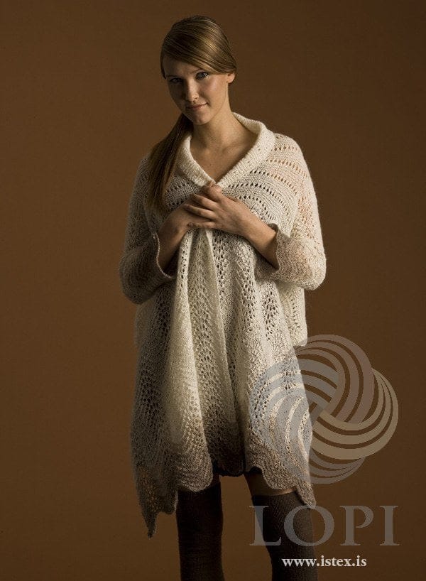 Woman holding the Faðmur lace wrap round her — white feather-and-fan lace shading to oatmeal at the ends