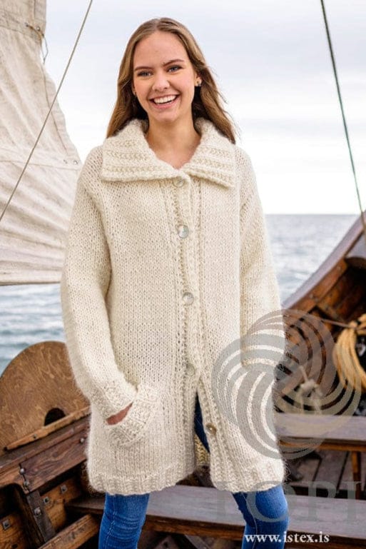 Smiling young woman on a boat in Júní, buttoned, one hand in a pocket — the white cardigan with its deep rib collar and ribbed front bands. The blue jeans and the earrings are not part of the pattern