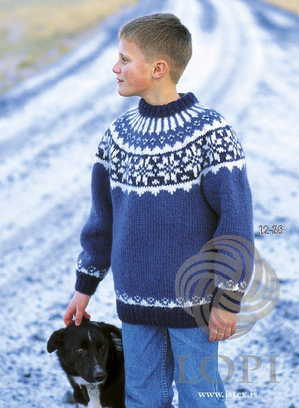 Boy with a black-and-white dog in the blue Lopi 12 no. 28 sweater — navy rib and folded neckband, a white band of navy star motifs on the yoke and white rays rising to the neck (shown in the original colours — this kit has blue tweed, with small white flecks, for the original blue 0098). The jeans are not part of the pattern