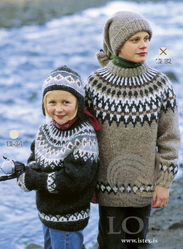 By the sea: the older boy, marked 12-32, in No. 32 — oatmeal heather with a yoke of a white zigzag, black heather diamonds and white spikes with an acorn-brown stripe across them, the same border above the hem and cuffs — and the long stocking hat, tied near the top with a dark cord, in the pattern’s own colours. Not part of this pattern: his green neck-warmer and dark trousers, and the sweater, hat, red neckerchief, fishing rod and jeans of the girl, marked 12-34, who wears a different pattern