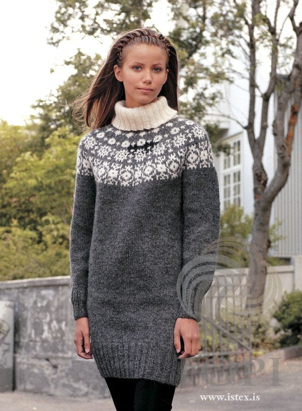 Woman in the grey Stafir sweater dress — dark grey heather with a yoke of white stars, a small black motif at the front and a white turtleneck. The black tights are not part of the pattern
