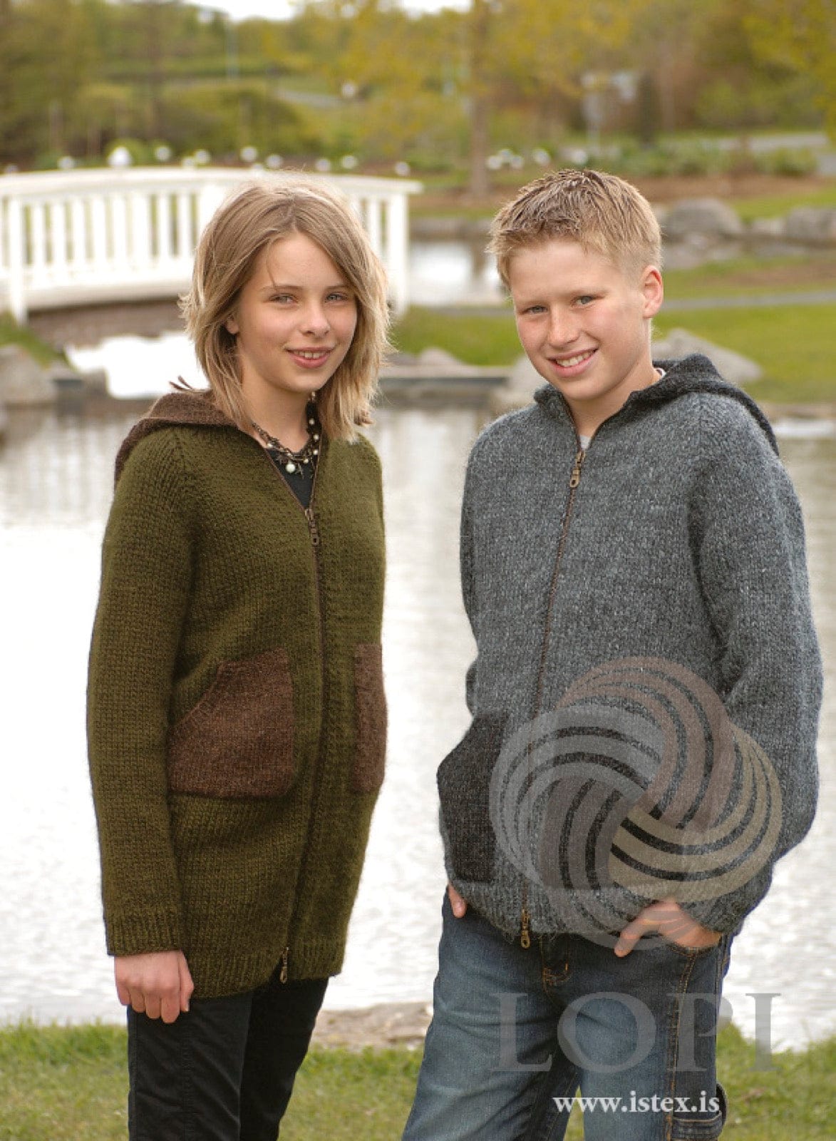A girl and a boy by a pond in B&G hoodies, both in the pattern’s own colours. She wears the long version in dark olive with a chocolate hood and patch pockets, reaching her upper thigh; he wears the short, hip-length version in dark grey with a black hood and pockets. Both close with a zipper up the front. Her black top, necklace and trousers and his jeans are not part of the pattern