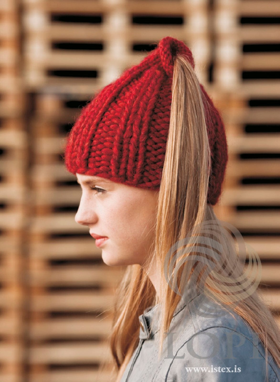 Woman in the Strompur hat — chunky carmine red Plötulopi rib with her ponytail through the open, rolled top