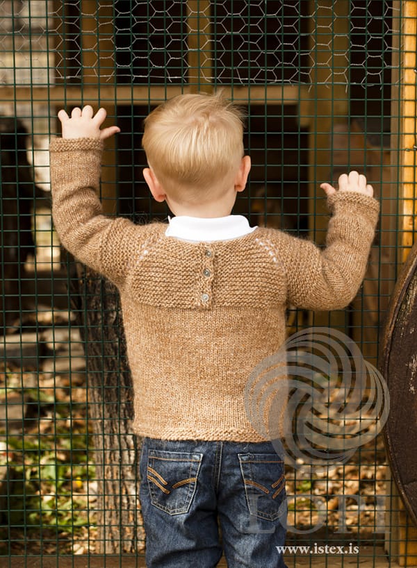 Kjarr in barley from the back — the opening at the back of the garter yoke closed with three buttons (not included), and small eyelets along the raglan lines, in the pattern’s original colour. The white collar of his shirt and his jeans are not part of the pattern