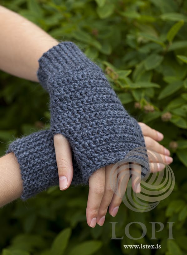 The María fingerless mittens in stone blue, worn on both hands — a garter-stitch band at the wrist, crochet over the hand and an open thumb hole, in the pattern’s original colour