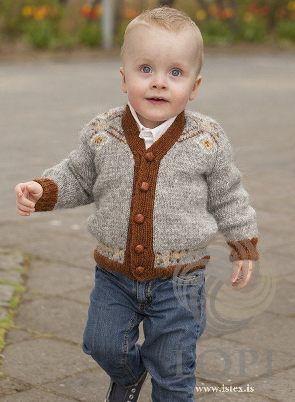 Toddler in the grey Norður cardigan — light grey with rust heather rib, bands and cuffs, rust diagonal lines and small yellow diamonds on the upper fronts, and five buttons, which are not included (shown in the original colours — this kit has mimosa in place of the sun yellow)
