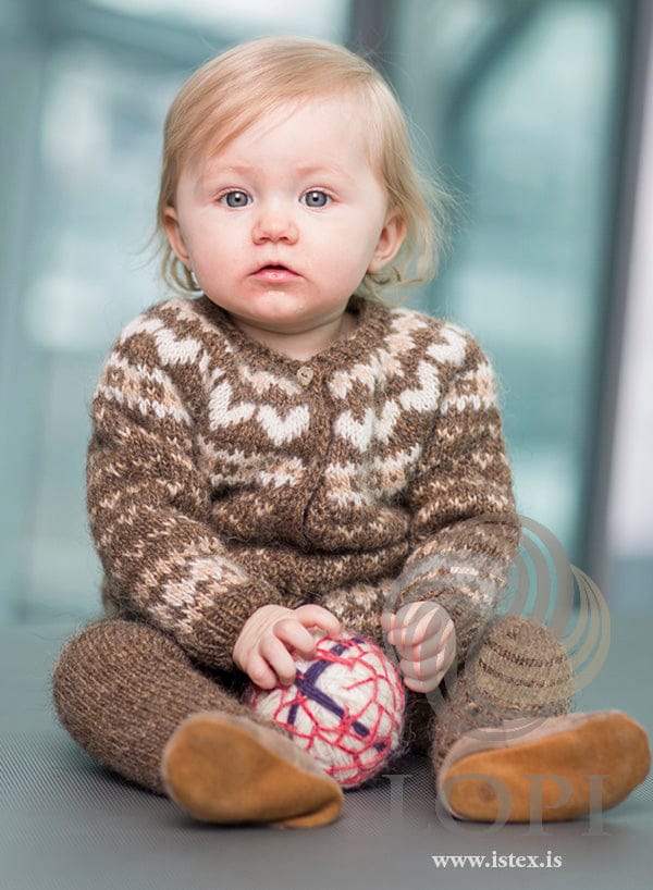 Baby sitting in the Hjörtu set — murky Léttlopi cardigan with straw and white hearts, and matching murky trousers
