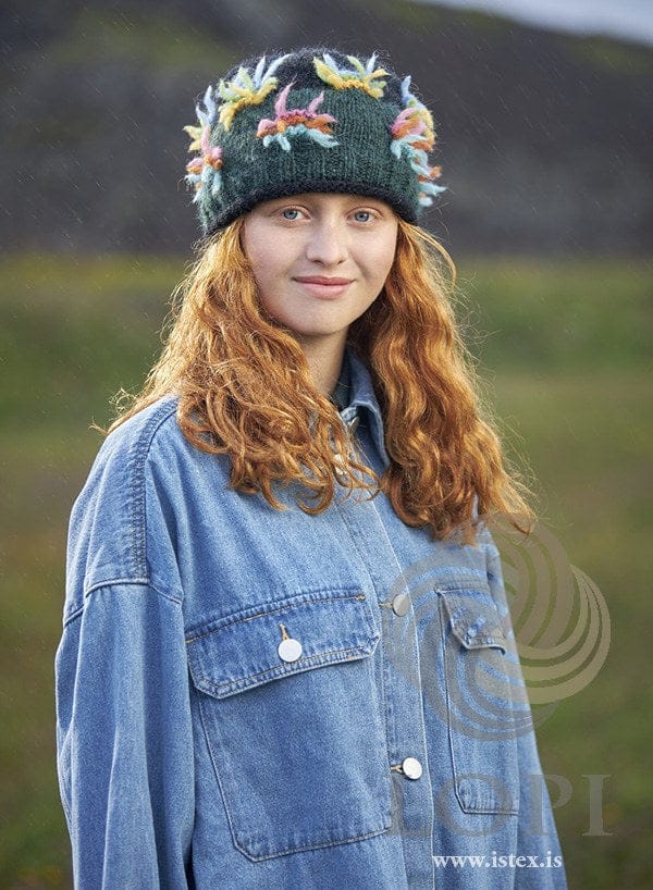 Young woman in the dark Lausn hat — bottle green with tufts of colour, a black top and a black rolled brim — the pattern cover
