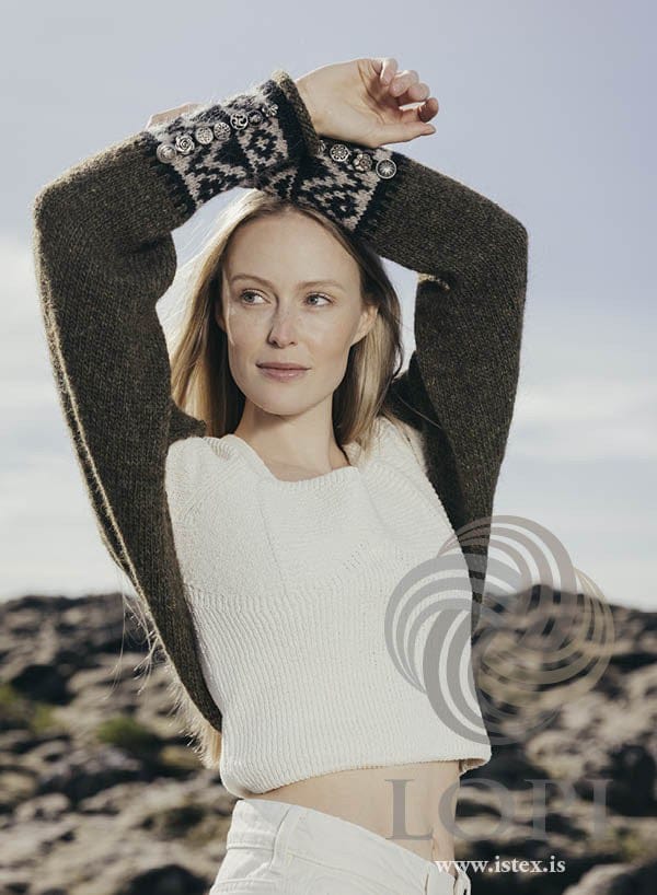 Woman with her arms raised in the moss green Armur shrug — patterned black and beige cuffs on dark moor green