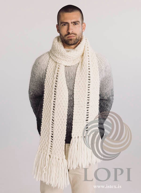 Stigi looped once round the neck with both ends hanging long, showing the eyelet ladder and the fringes at both ends, in white Jöklalopi. The shaded grey sweater and the light beige trousers are not part of the pattern