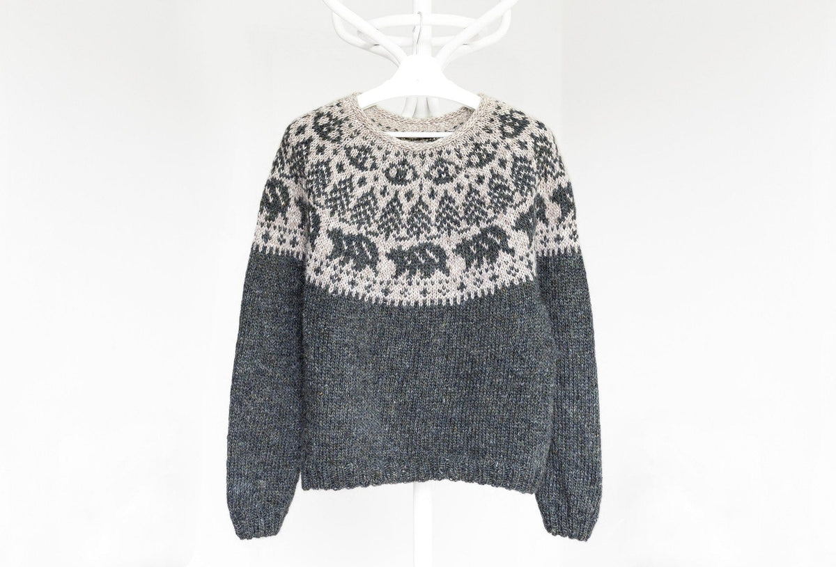 Mishka Lopapeysa on a hanger: dark grey-green Rough Sea body and sleeves with k2, p2 rib, and a light beige yoke with walking bears and fir trees