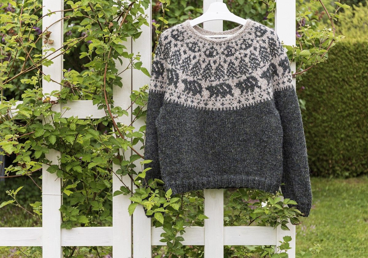 Front view of the Mishka Lopapeysa on a garden trellis, showing the bear and tree yoke and the ribbed hem and cuffs