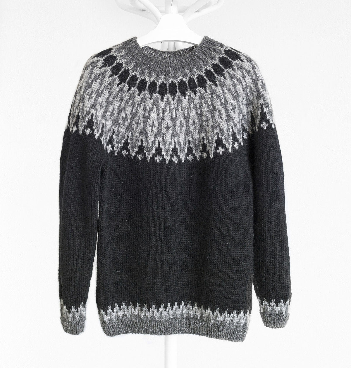The black and grey Odin Lopapeysa on a hanger: black body and sleeves, an ash and dark grey yoke with a ring of black drops, and dark grey rib