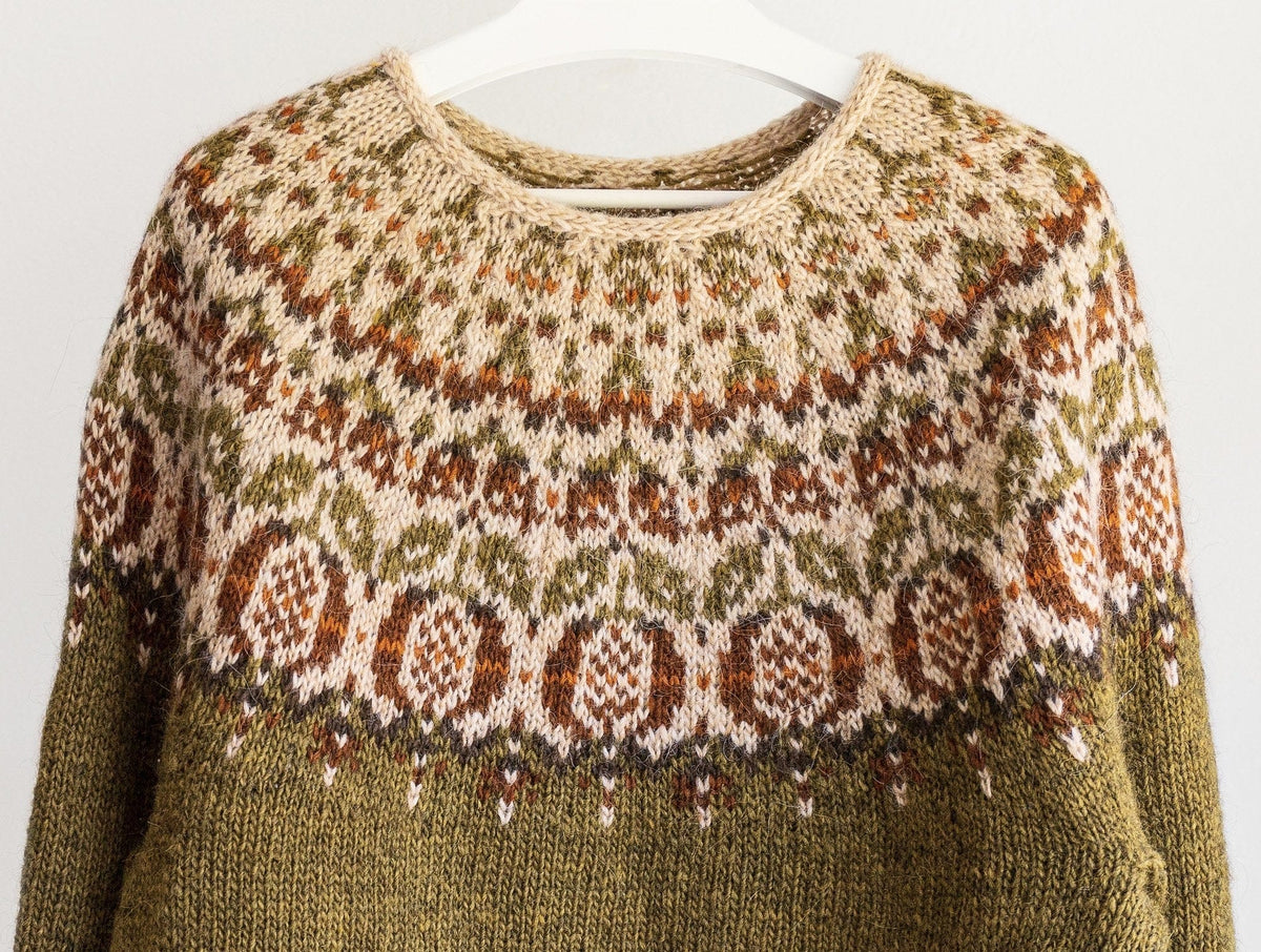 Close-up of the Pomegranate yoke: rust pomegranates with checked seeds and an apricot stripe, olive leaves, small fruits and a straw i-cord neckband