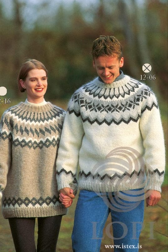 Smiling man holding a woman’s hand, wearing No. 6, the white version of this pattern, in its own colours — white with pale grey rib, a dark grey zigzag border above the rib, a yoke with a dark grey zigzag edge, a pale grey band of dark grey X shapes and diamonds, and dark grey lines on pale grey up to the neckband. “12-06” is printed on the photo. His grey collar and jeans are not part of the pattern; the woman wears Lopi 12 no. 16, a different pattern, with a white polo neck, an earring and dark leggings