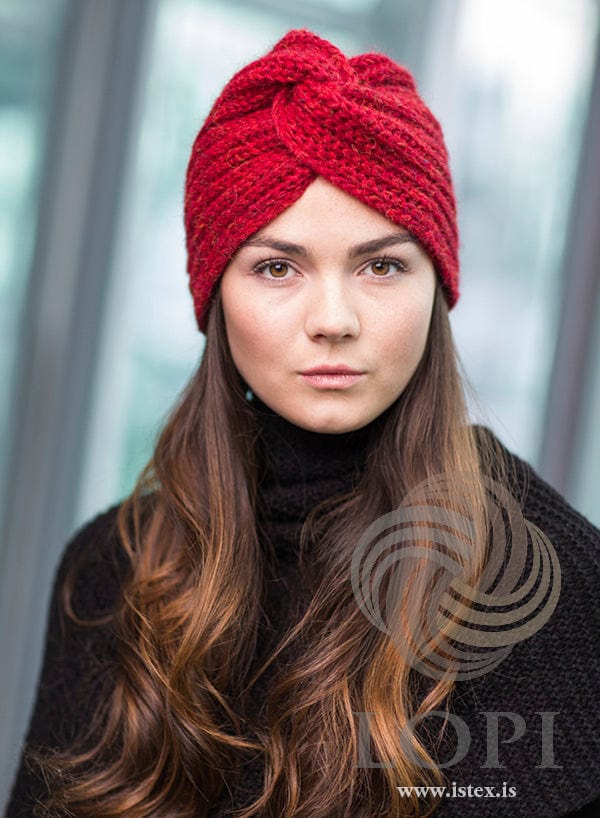 Front view of Höttur in carmine red heather — the strip twisted into a knot at the centre front, with brioche ribs at each side. The black polo neck and the black knitted top are not part of the pattern