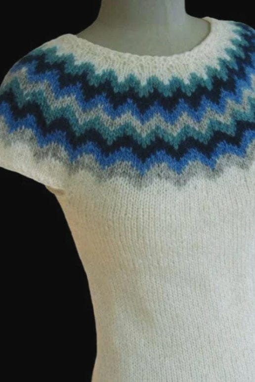 Vormorgun on a dress form against a black background, shown in the pattern’s own colours — a white Léttlopi top with short caps over the shoulders and a round yoke of zigzag stripes in ash, heaven blue, lapis blue and glacier blue, twice over, with a white band below the neck. The dress form is not part of the pattern