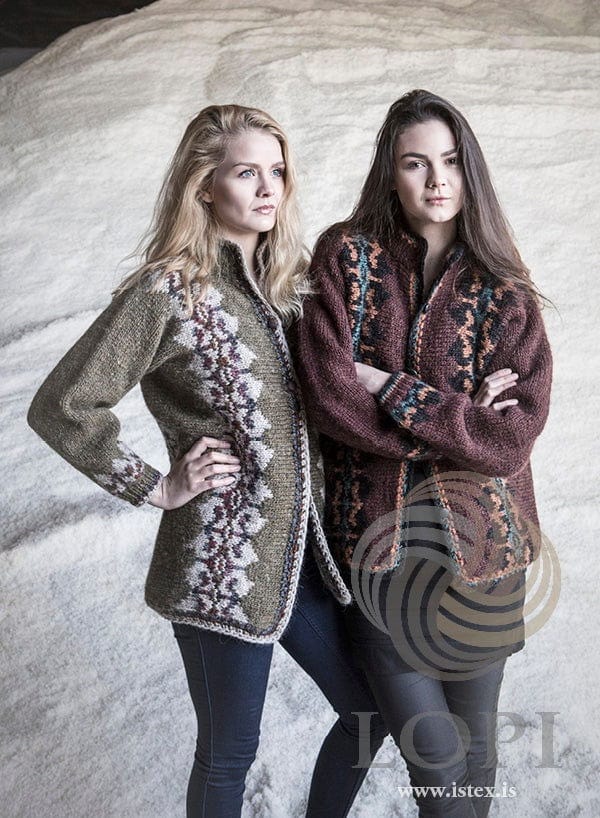Two women in the two Lilja colourways, shown in the pattern’s original colours (the green version’s rose heather is no longer made) — on the left the green cardigan, buttoned, with light beige bands of dark multicoloured motifs down the front and near the cuff; on the right the auburn one, sheep sorrel with black bands of teal and amber motifs. The dark jeans, the black top and dress and the black leggings are not part of the pattern