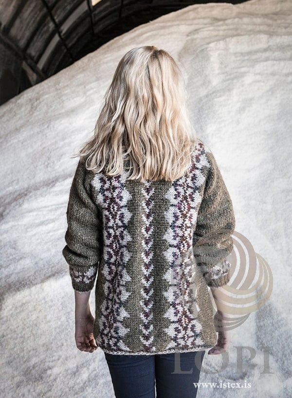The green Lilja from the back, shown in the pattern’s original colours (rose heather is no longer made) — a narrow dark band down the centre back between two light beige bands with dark motifs. The dark jeans are not part of the pattern