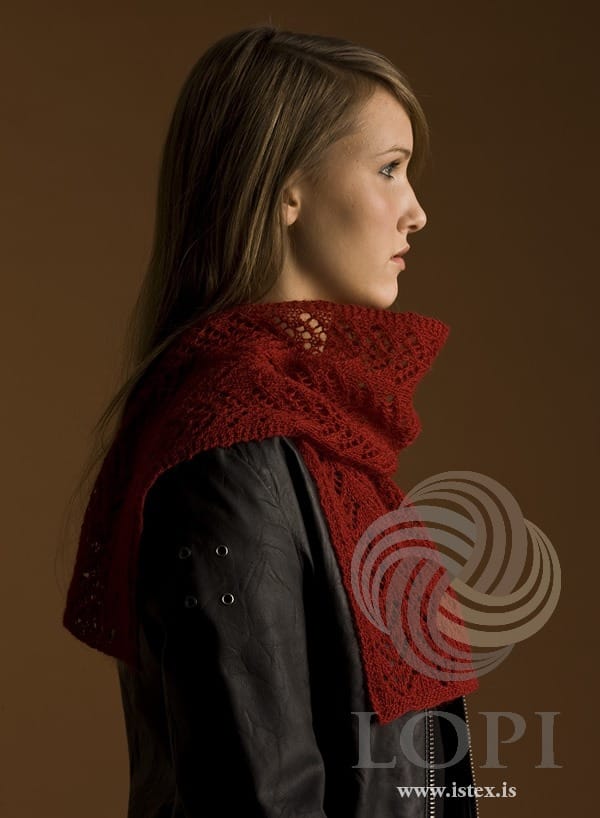 Young woman in profile wearing Strik round her neck, shown in the pattern’s own colour, red Einband — the lace of V shapes in eyelets and the garter-stitch edges, one end hanging down in front. The black leather jacket is not part of the pattern