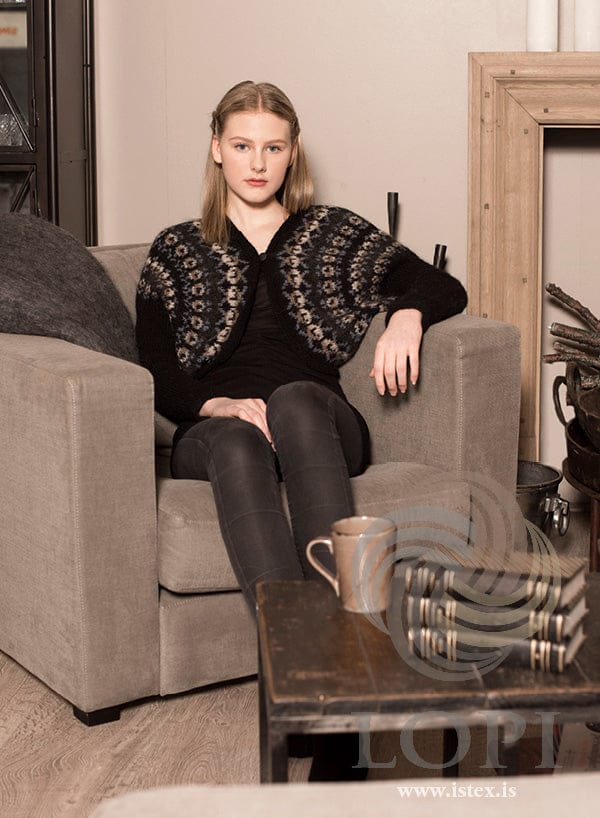 Heartwarmer shrug in black Léttlopi with blue roses, worn seated over a black top