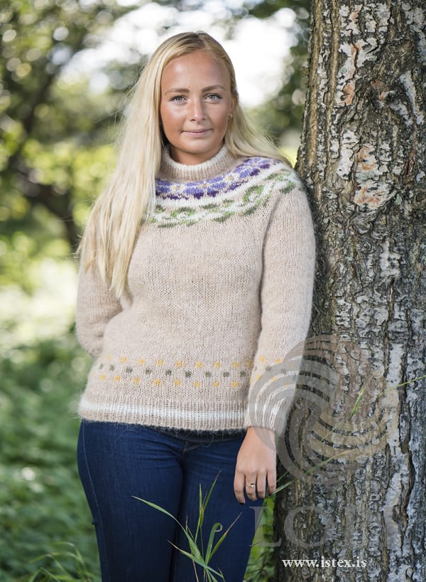 Manitoba from the front, worn leaning against a tree — the flower yoke, the dotted border above the striped hem rib and the straw body, in the pattern’s original colours. The jeans, earrings and ring are not part of the pattern
