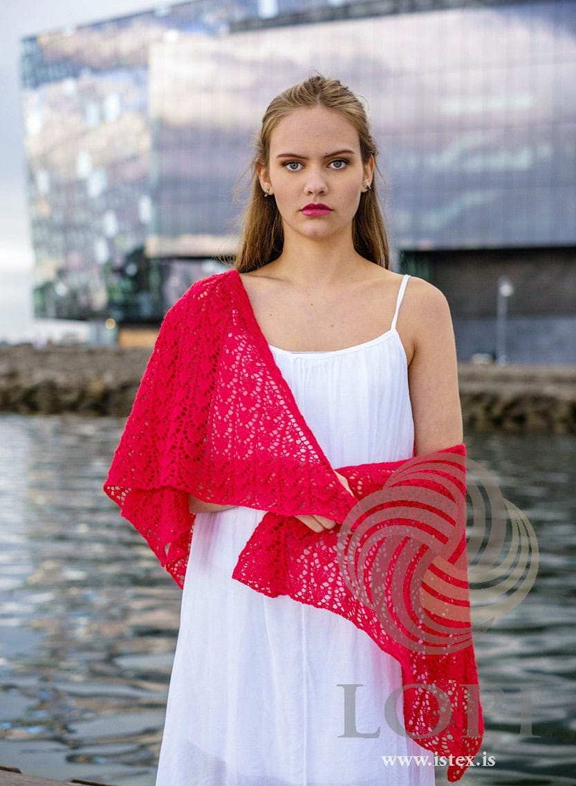 Túlipanar worn over one shoulder and draped across the front over her arms, flame red Einband lace in the pattern’s original colour. The white dress and her earrings are not part of the pattern
