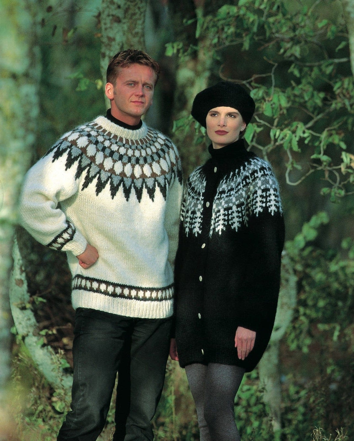 Woman among trees in the Lopi 12 no. 2 cardigan and beret, shown in the pattern’s own colours — a long black cardigan to mid-thigh with a round yoke of white tree motifs and grey heather and white bands above them, six pale buttons down the front, and a black beret. The tall black polo collar at her neck, her grey tights and the man’s white yoke sweater (Lopi 12 no. 22, a different pattern) are not part of this pattern