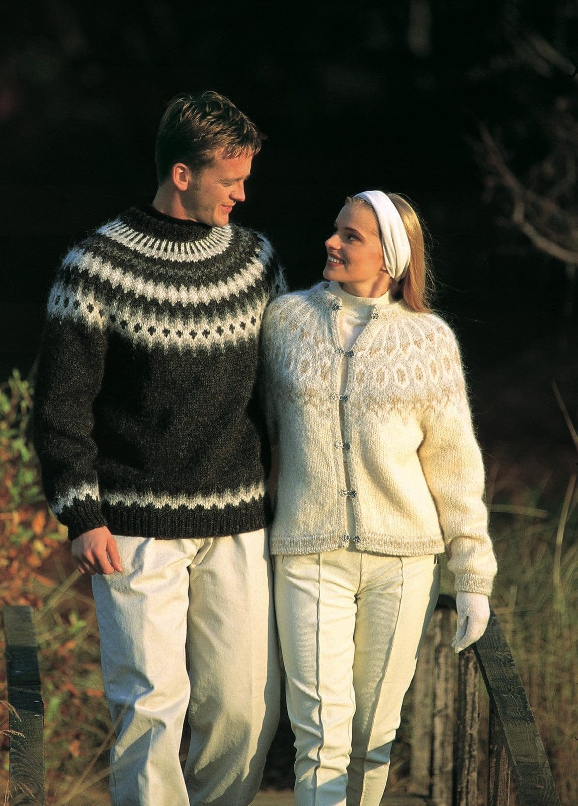 Woman in the white Lopi 12 no. 8 cardigan, with light beige and light ash motifs on the yoke, patterned borders and six silver-tone clasps; the man’s dark sweater is Lopi 12 no. 20, a different pattern