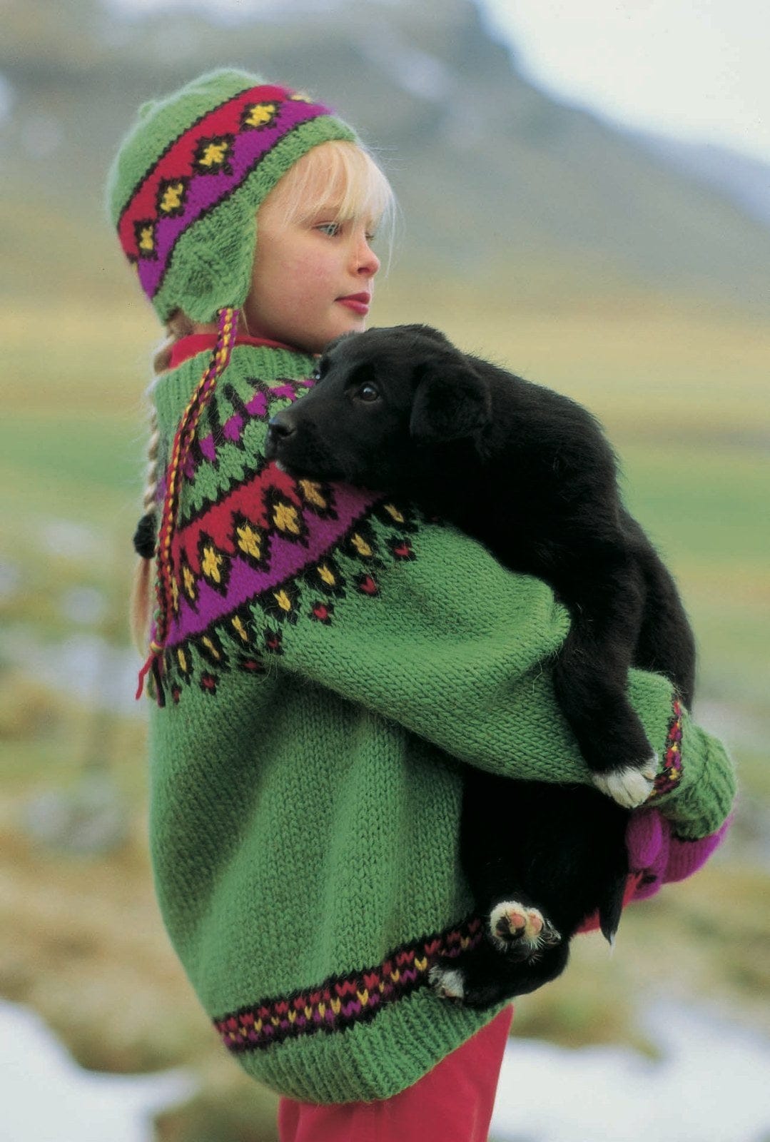 The same set in its bright version, No. 33 — a green sweater and ear-flap hat with a magenta, red and gold yoke — on a girl holding a puppy; sold as a separate kit, with four colours replaced