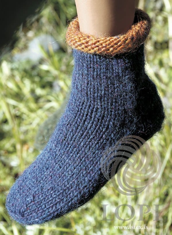 One Uni ankle sock on a foot against sunlit grass — plain stocking stitch in a deep blue heather with a rolled amber top edge, a plain foot and a blunt toe, shown in the pattern’s original colours: sapphire blue heather (9968, no longer made) and amber heather (9971)