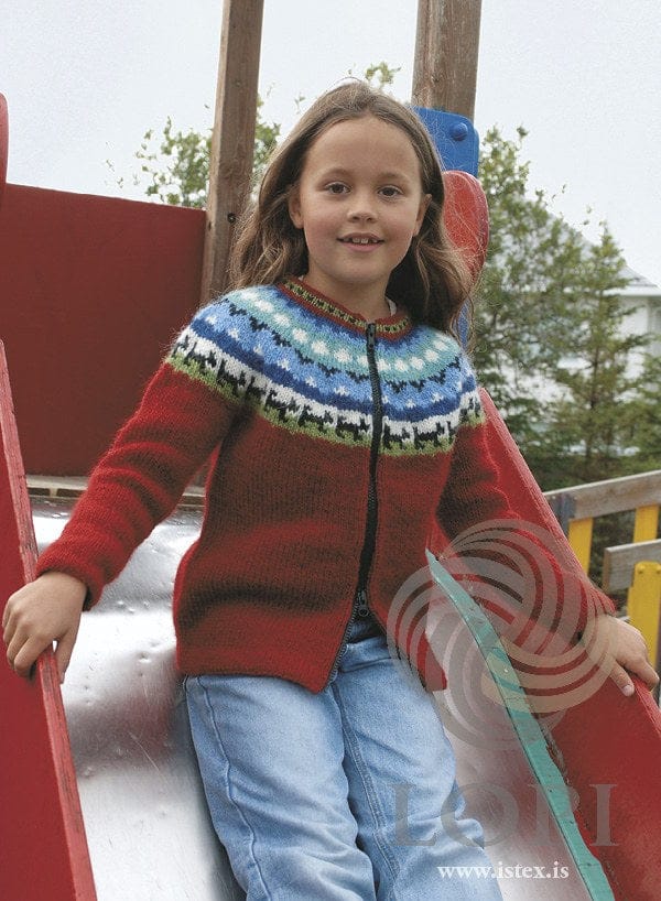 Girl on a playground slide in the red Lappi zip cardigan — crimson with a yoke in spring green, black, white and blues