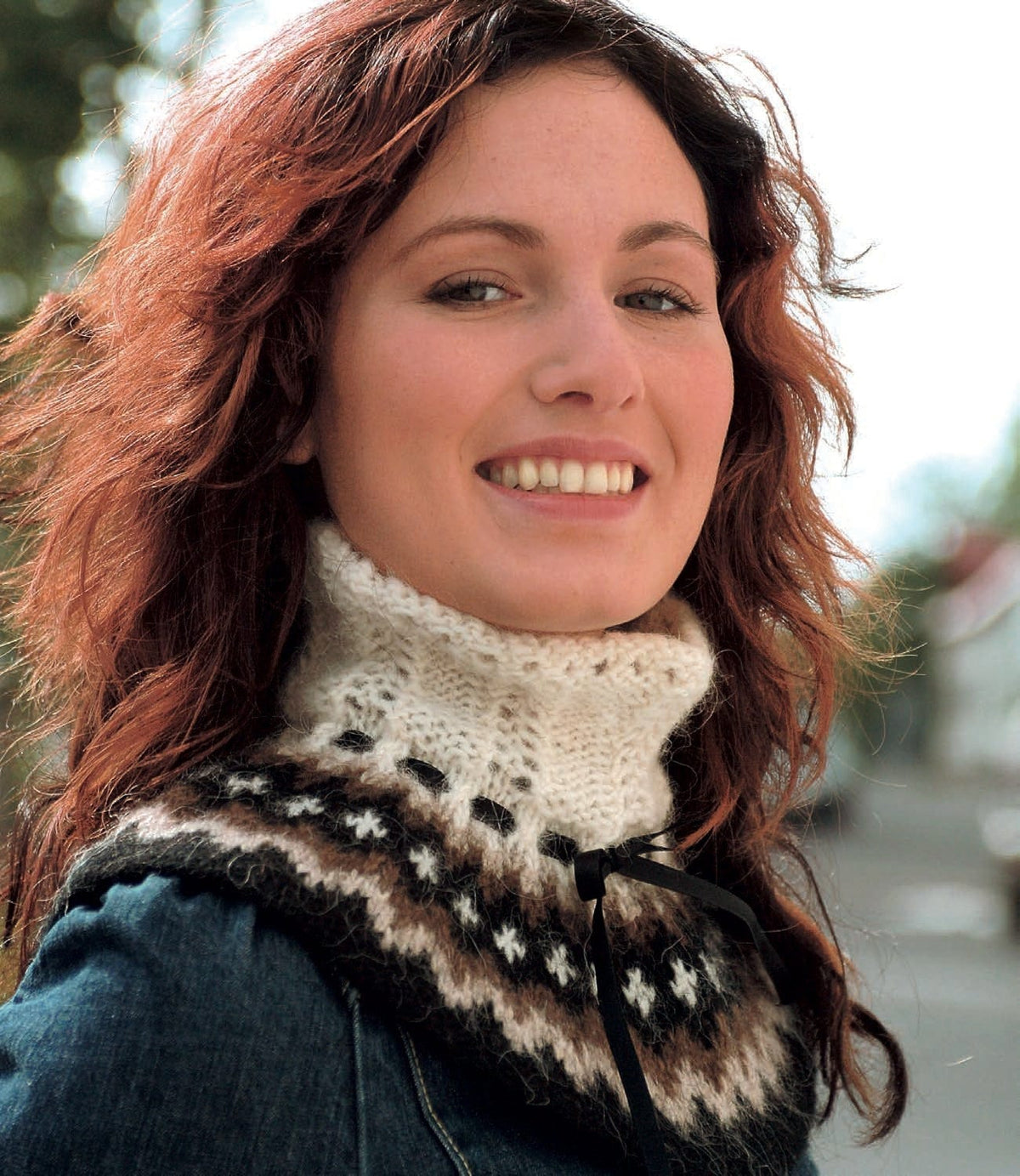 Woman wearing the Rjúpa collar over a denim jacket — light beige and acorn zigzags with white crosses on black over the shoulders, a white lace turtleneck and a black ribbon tied at the neck