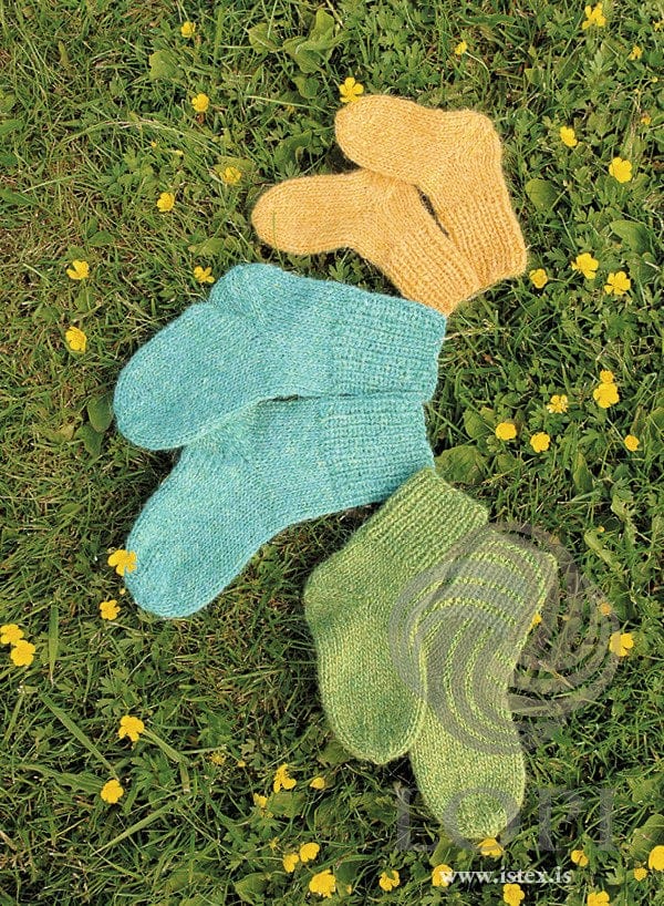 Three pairs of Sokkar children’s socks on grass — this kit is the yellow pair at the top right (shown in the original colour — this kit has mimosa in place of the sun yellow); the turquoise and green pairs are sold as separate kits
