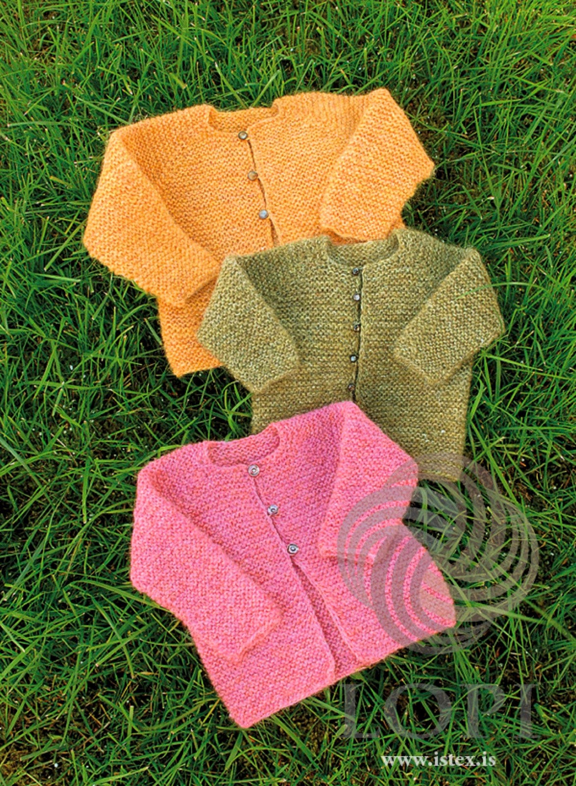 Three Ungi baby cardigans laid on grass — golden yellow, clover green and sunset rose garter-stitch Plötulopi with small buttons