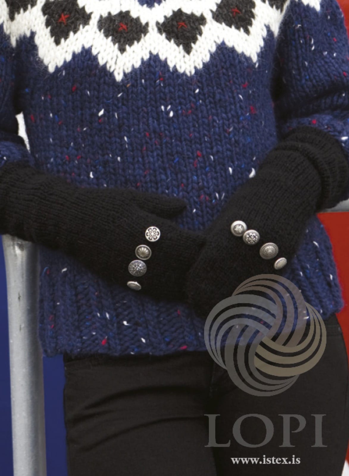 A woman’s hands in Happ — black Léttlopi mittens, each with four silver-tone buttons of different designs in a line at the wrist, the long cuffs pushed up the arms, shown in the pattern’s own colour. The navy flecked sweater with a patterned yoke is a different pattern, and the black trousers are not part of the pattern either