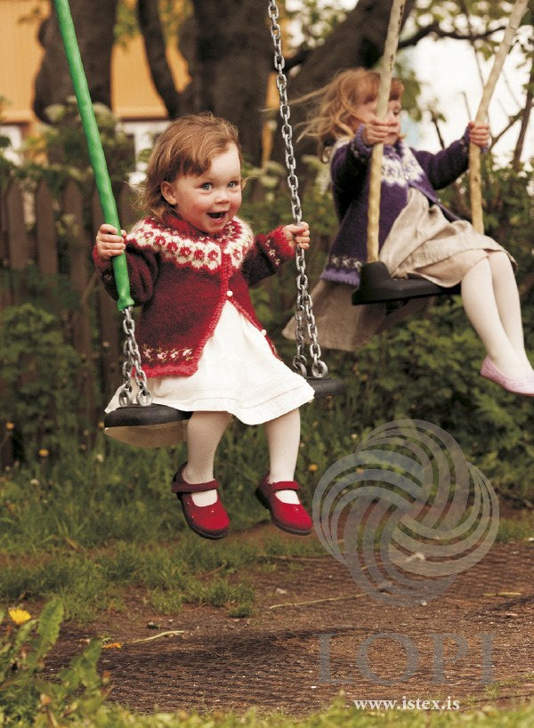 Girls on swings: the red Knúpur on the toddler in front, the purple version on the girl at the back, sold as a separate kit (shown in the original colours — this kit has crimson red in place of the light red). The dresses and shoes are not part of the pattern