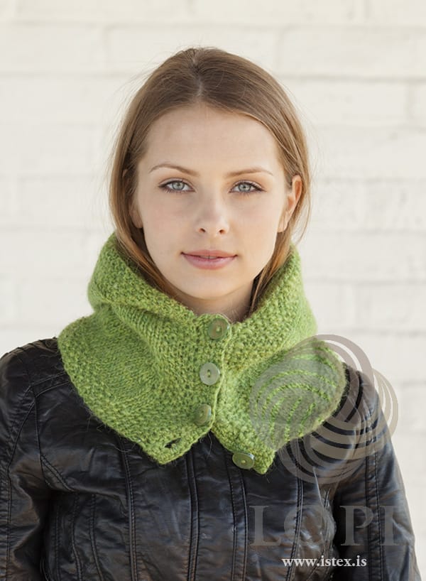 Hetta in spring green heather worn down round the neck as a buttoned collar, showing the moss-stitch edges and the four buttons down the front. The black leather jacket is not part of the pattern