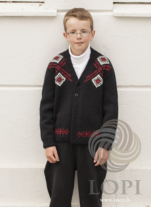 Boy in the black Norður cardigan — a V-neck, brick red diagonal lines and white-framed red diamonds across the upper fronts, and a red border of crosses above the hem rib; the white turtleneck is not part of the pattern