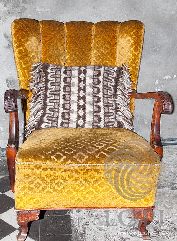 Fregn cushion in chocolate, ecru and oatmeal heather Álafosslopi with a fringe, on a gold velvet armchair