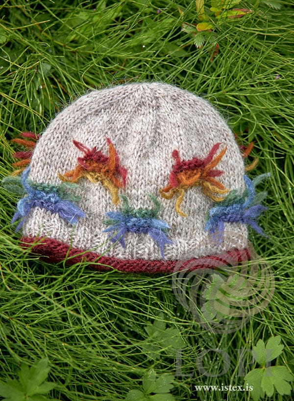 Lausn hat in light beige Léttlopi with tied tufts of colour, lying in the grass