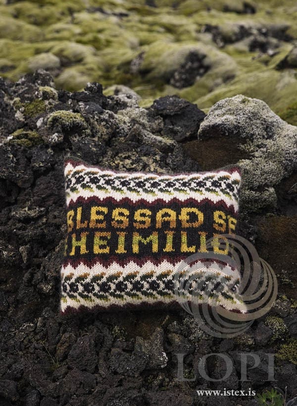 Blessun cushion in Álafosslopi reading BLESSAÐ SÉ HEIMILIÐ, on mossy lava