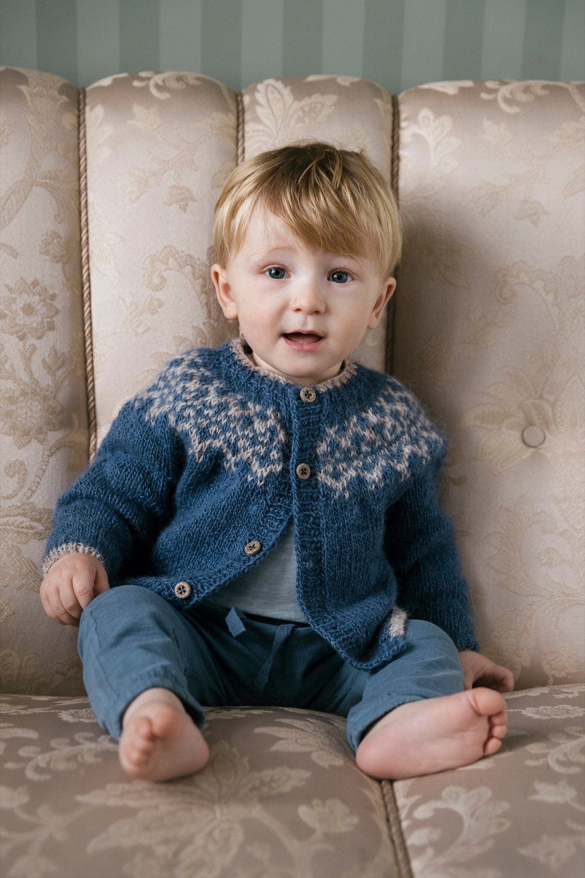 Dagmál baby cardigan knitted in Fjallalopi — mountain blue with a light moorit yoke pattern and buttons