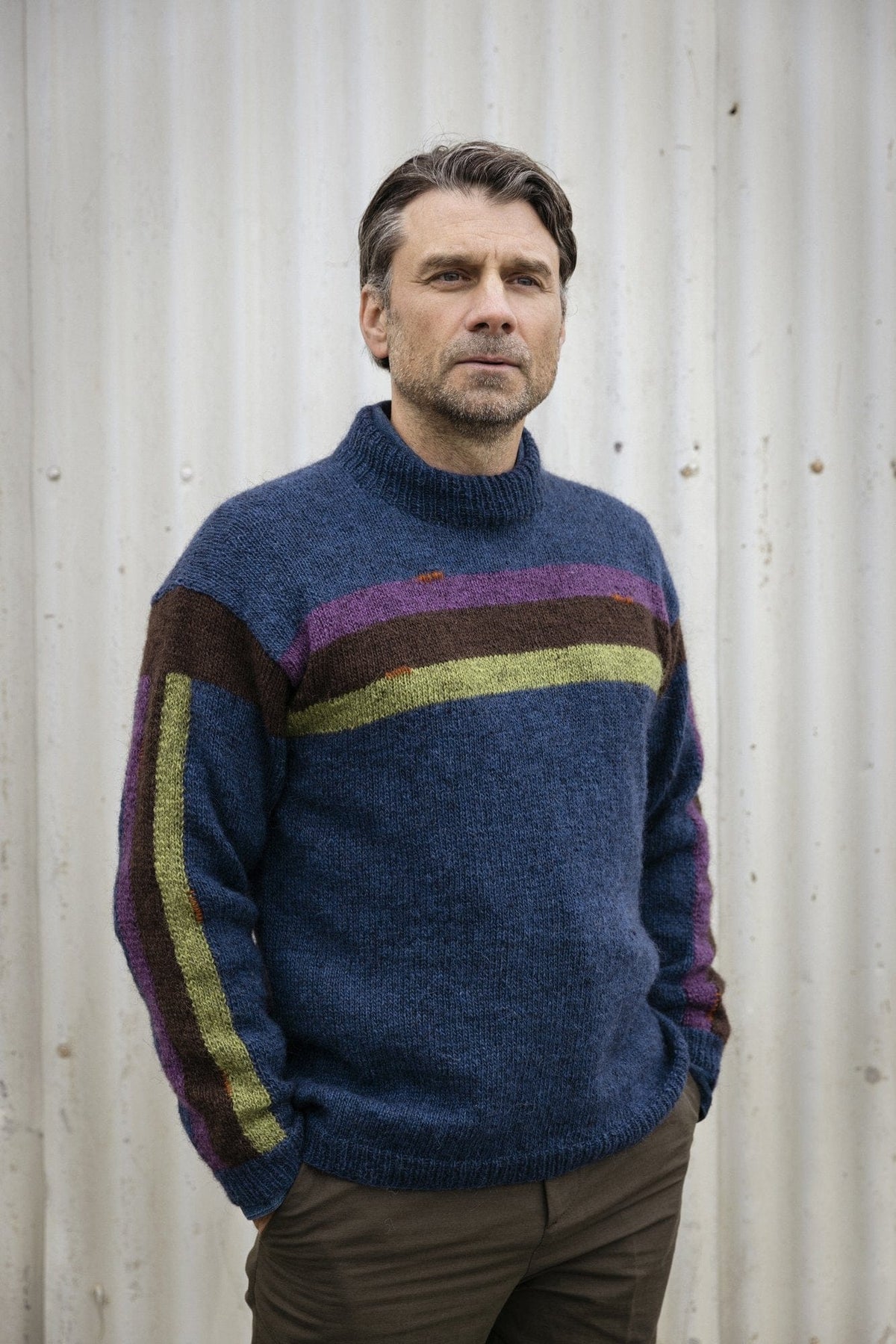 Kilir sweater knitted in dusk blue Fjallalopi with moss, brown and purple stripes across the chest and down the sleeve