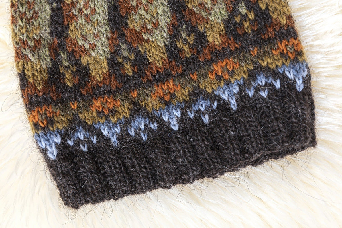 Close-up of the Lofoten Hat brim: k2, p2 rib in black sheep heather, a light blue and stone blue band, and small apricot and golden motifs